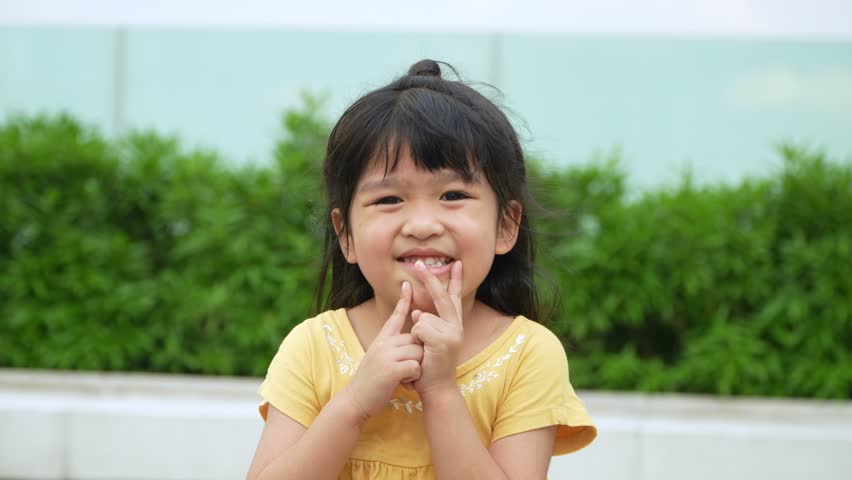 Portrait Funny little asian girl big smiling child looking at camera and pointing her cheeks, enjoying childhood testimonial concept, Positive child, 4k footage, Slow Motion Portrait