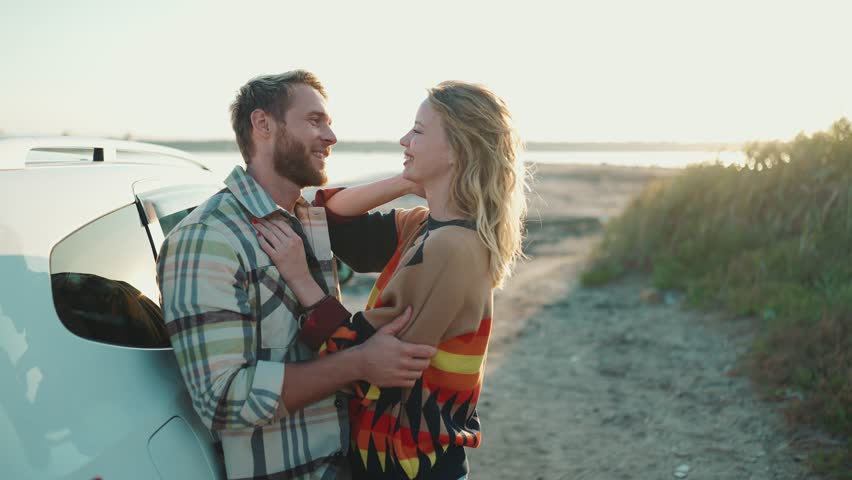 Smiling blond couple talking and hugging near car outdoors