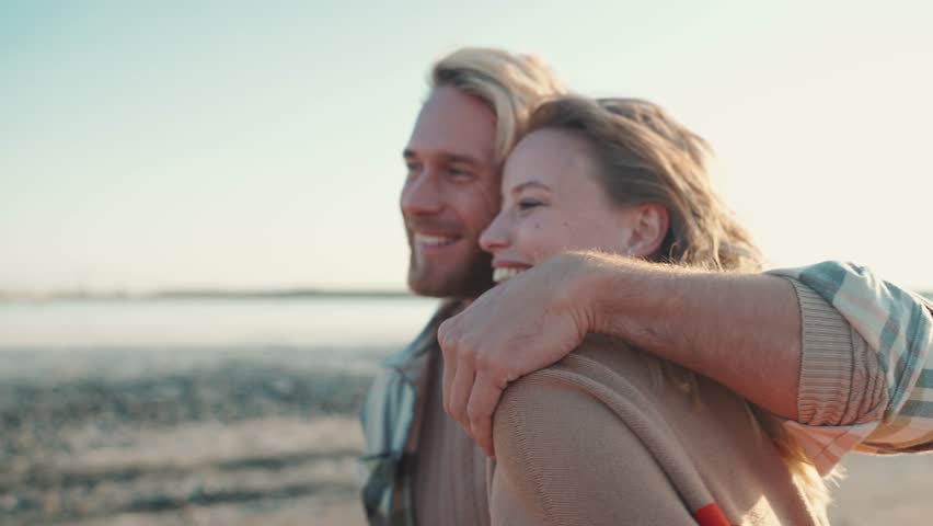 Positive young blond couple hugging and walking near estuary outdoors