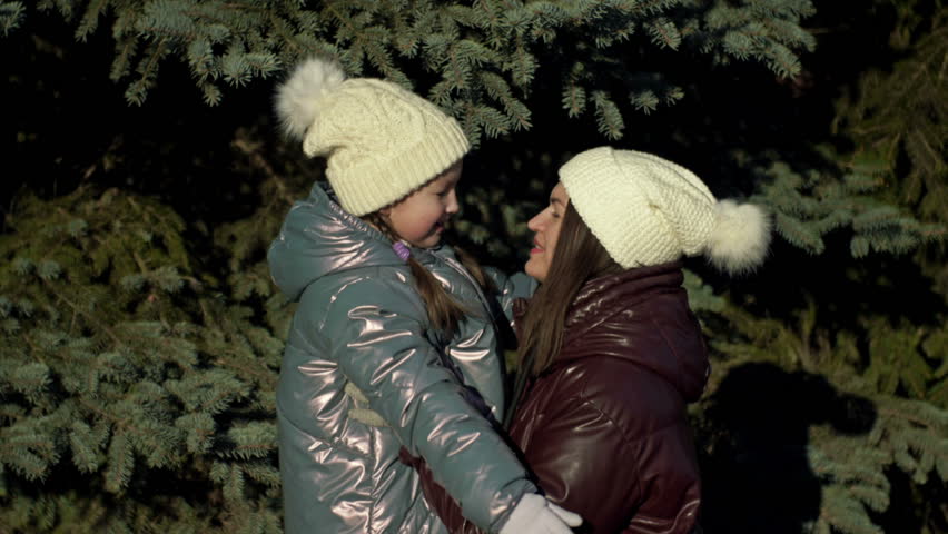 Young woman and her daughter, 7-8 years old, look at each other with love and tenderness. On a walk in the winter forest.