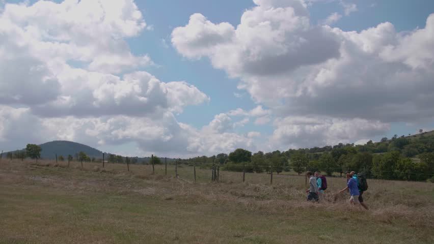 A slow-motion of hiker friends walking in the countryside field against a clouded sky