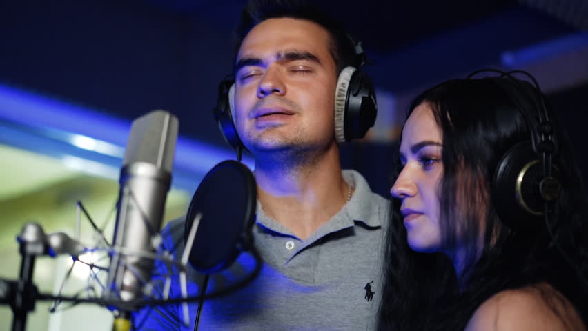 Couple recording a song in the studio. Duet singing emotionally in front of professional microphones. | Shutterstock HD Video #1099357611