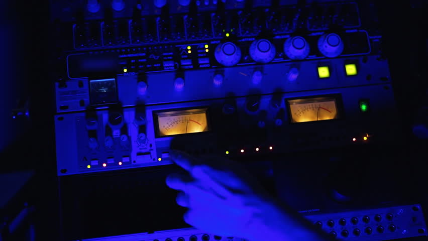 Studio recording equipment in the blue light. Male audio engineer’s hand working on the stereo panel. Top view close up. | Shutterstock HD Video #1099357641