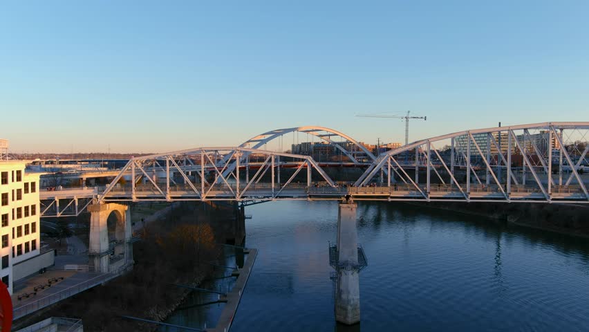 Nashville Tennessee USA - 1 16 2023: aerial footage of the John Seigenthaler Pedestrian Bridge with people walking along the bridge surrounded by the Cumberland River, winter trees and blue sky Royalty-Free Stock Footage #1099363385