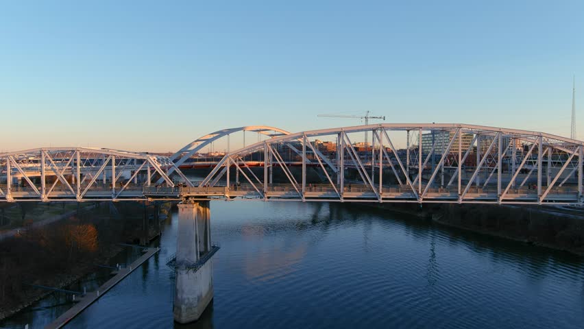 aerial footage of the John Seigenthaler Pedestrian Bridge with people walking along the bridge surrounded by the Cumberland River, winter trees and blue sky in Nashville Tennessee USA Royalty-Free Stock Footage #1099363865