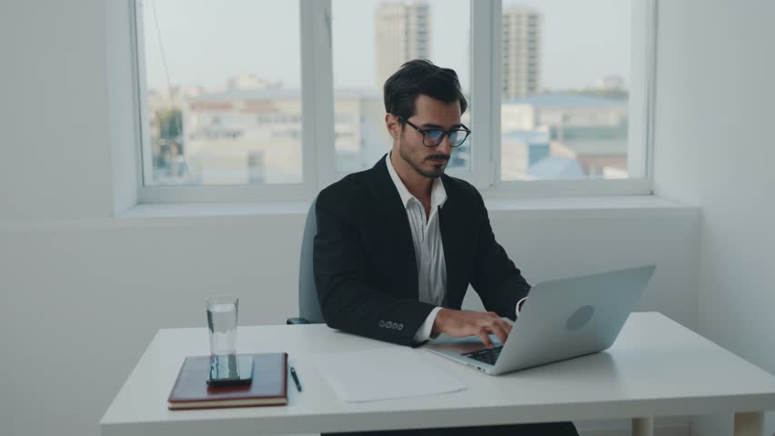 Man in business suit and glasses working in office typing laptop text on desk at workplace, online working at computer and papers documents.  | Shutterstock HD Video #1099363917