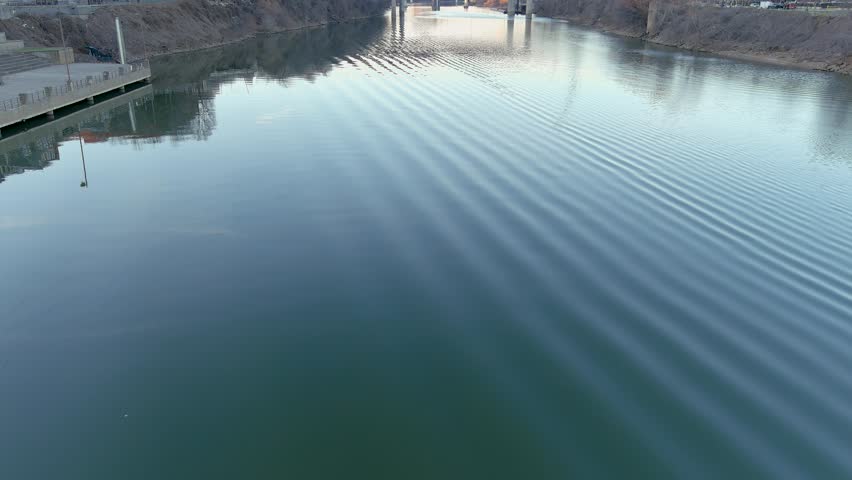aerial footage along the rippling green waters of the Cumberland River with a bridge over the water and buildings along the riverfront in Nashville Tennessee USA