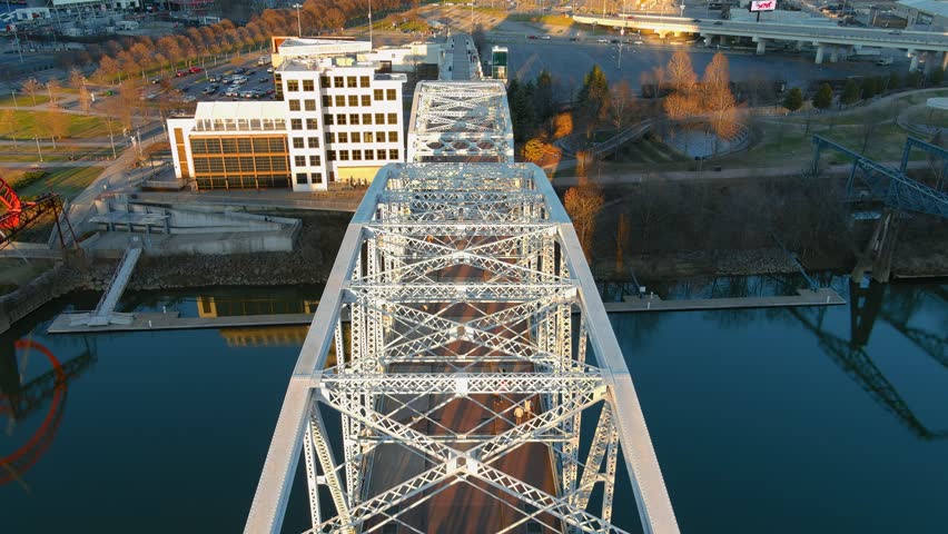 aerial footage of the John Seigenthaler Pedestrian Bridge with people walking along the bridge surrounded by the Cumberland River, winter trees and blue sky in Nashville Tennessee USA Royalty-Free Stock Footage #1099365407