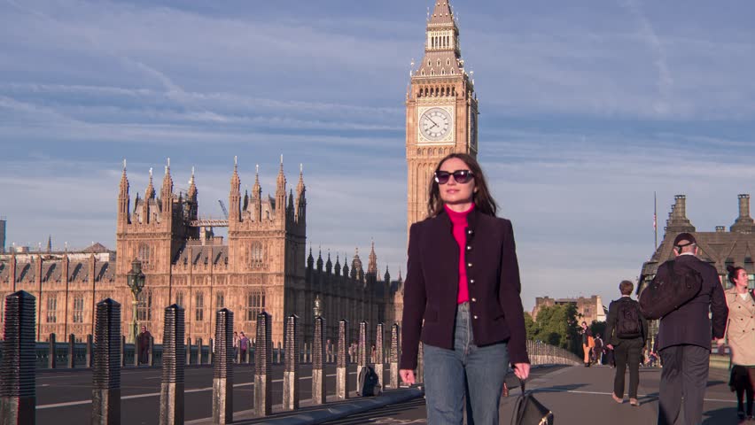 Attractive European looking woman walking on Westminster Bridge London with smiling, smirking face. Stylish trendy businesswoman having a walk on Westminster Bridge on a morning crowded day Royalty-Free Stock Footage #1099367335