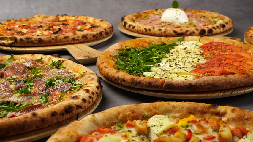 Many kinds of Italian Hot and Tasty Pizza on the table. Big Sizes Pizzas at the Kitchen. Italian Dishes. Pizza with Herbs, Pepper, Sausage, Melted Cheese. Well Baked Dish. Close-up of a freshly baked 
