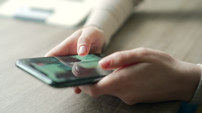 Close-up of a female's hand scrolling through a social network while holding a smartphone. Young woman using browsing mobile phone indoors | Shutterstock HD Video #1099370583
