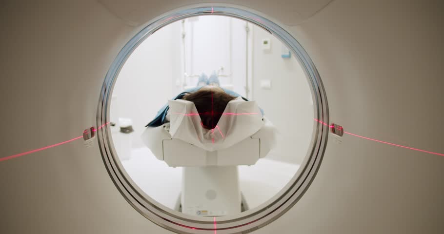 Woman during CT scanning procedure. Tracking shot of female patient lying on table sliding into CT machine near crop doctor in laboratory of modern clinic.Modern technologies.Shot Of CT Scanning Room. Royalty-Free Stock Footage #1099371681