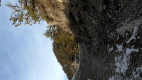mountain unicyclist downhilling a trail with some snow. Background is composed of forest and blue but cloudy sky. Vertical video with copy space in 60 fps good for slow motion and social media