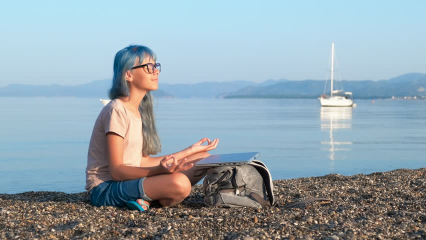 Millenial girl on beach with laptop. A view of millenial girl with notebook against sea scape. A concept of summer studing time during sea traveling.