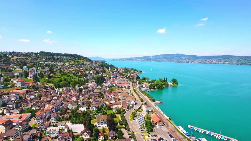 Aerial shot of the blue sky and ocean, and the beautiful Swiss town at shore | Shutterstock HD Video #1099377373