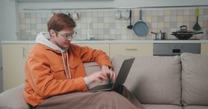 Young blogger makes plan for future video content on laptop. Red-haired man wearing glasses pays attention to details for videos on device