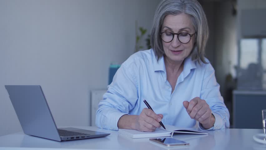 Positive retired lady writing down to do list for vacations smiling and dreaming | Shutterstock HD Video #1099385271