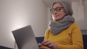 Happy mature woman making video call using web camera and special application on her laptop to communicate with foreign relatives, way to be closer and see each other, wifi connection