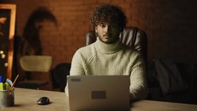 Front view of a man working with laptop at his desk. Freelancer with curly hair using computer at home office. Distant work, e learning, freelance job