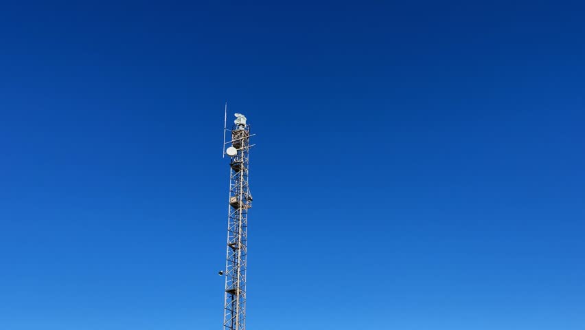 Radar tower with spinning antennas and surveillance camera against blue sky