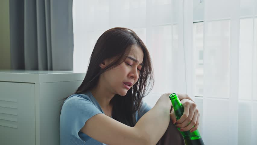 Asian young depression woman feeling heart broken and drinking beer. Attractive beautiful girl sitting on floor holding a bottle of alcohol feeling loneliness, drunk and hangover alone in living room. Royalty-Free Stock Footage #1099390161