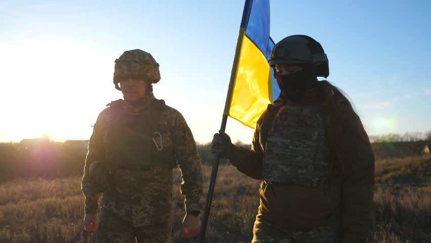 Soldiers of ukrainian army walks at field with flag of Ukraine. People in military uniform waving national yellow-blue flag as sign of victory against russian aggression. Invasion resistance concept Royalty-Free Stock Footage #1099390809