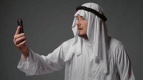 Authentic muslim businessman in traditional white kandura with beard using smartphone. Successful Saudi, Emirati, arab businessman concept.