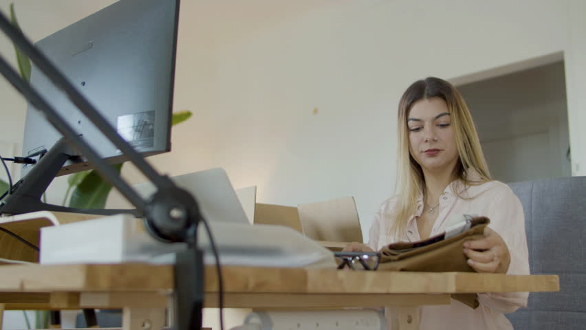 Young Caucasian woman checking clothing label and barcode on computer, and then packing item in cardboard parcel. Female webstore owner making delivery preparations. Startup, online store concept | Shutterstock HD Video #1099392227
