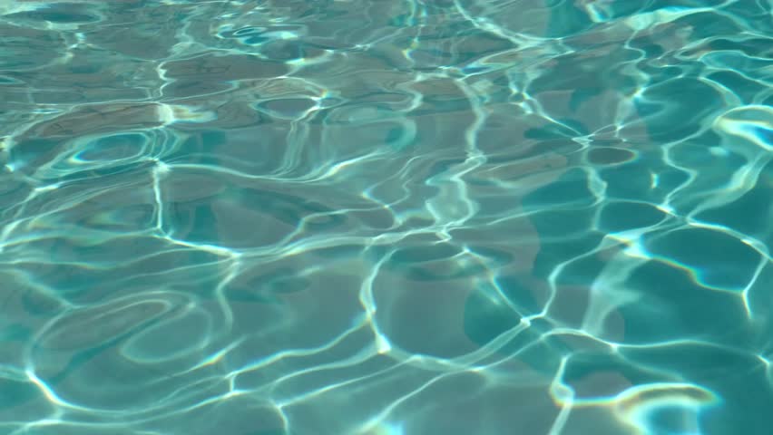 Pure light turquoise water in swimming pool with sun reflections. Rippled water surface background