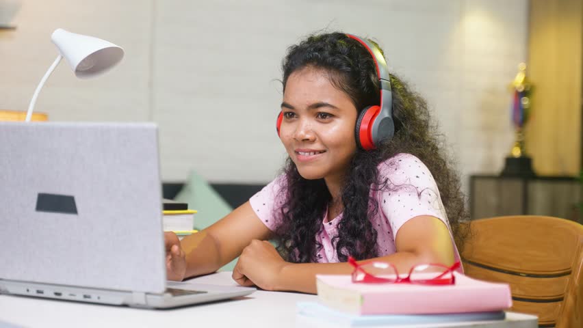 Girl enjoying music on wireless headphones while studying or during online class at home - concept of relaxation, stress relief and technology distraction.