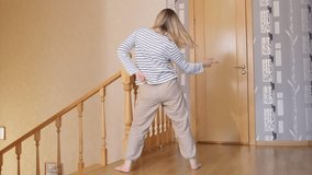 Girl fools around in bright apartment, joy, antics. Moving to a new apartment, completion of repairs. Foolish dance against the staircase, back view. High quality FullHD footage with slow motion