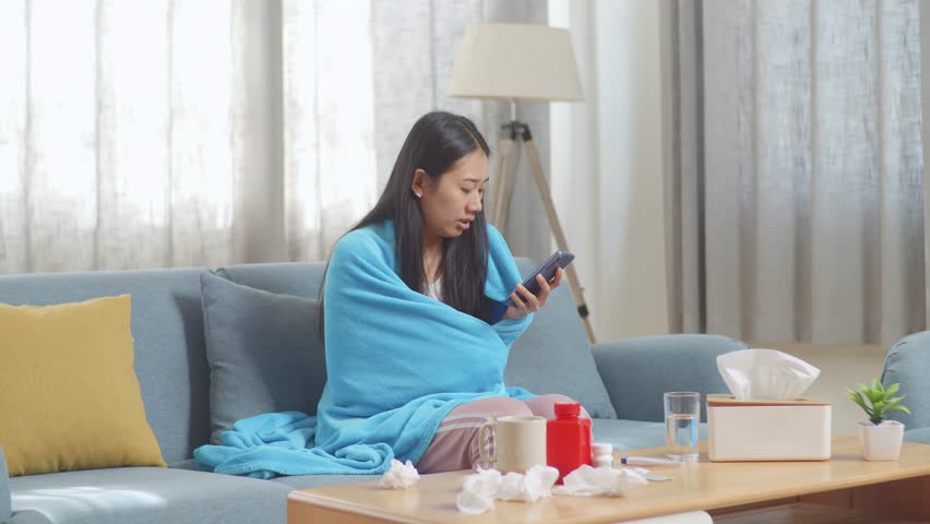 Asian Woman With Blanket Suffering From Cough While Talking On Phone With Doctor On Sofa In The Living Room At Home
 | Shutterstock HD Video #1099402895