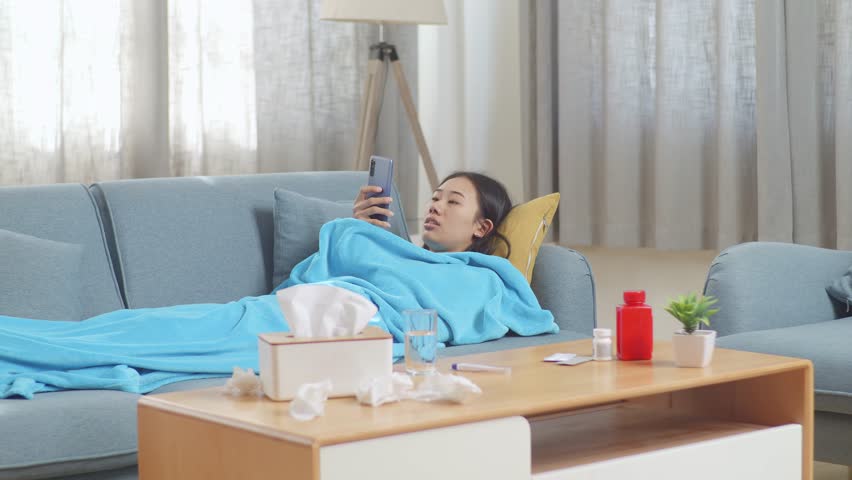 Sick Asian Woman With Blanket Freezing And Shiver While Talking On Phone With Doctor Lying On Sofa In The Living Room At Home
 | Shutterstock HD Video #1099402901