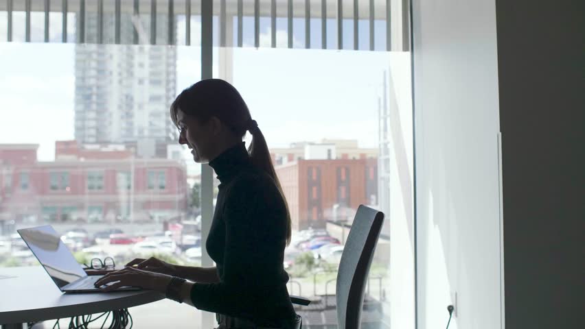 Smiling businesswoman working at laptop in urban office window | Shutterstock HD Video #1099404053
