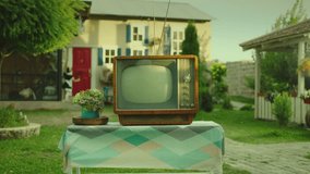 Retro style TV set . Old fashioned television standing on the table outdoors . Beautiful village house , garden on background . Vintage designed atmosphere . Fairy tale decoration . Grandma's house