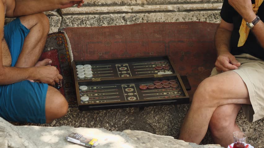 Close-up of two men playing backgammon on the street in Turkey. One man is smoking. A cup of tea is next to him. Backgammon for the street