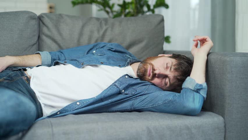 Portrait of drunk bearded man sleeping on the couch at home with a bottle next to him and has a severe hangover after big spree Alcoholism addiction and bad habits concept a exhausted person | Shutterstock HD Video #1099411683