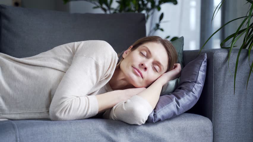 Serene young woman take break napping feel stress free sleeping on the couch in the living room Positive blond cute girl in a relaxing and resting lying on comfortable sofa at home  | Shutterstock HD Video #1099411743