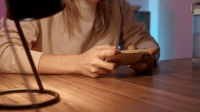 Close up cellphone. woman sits at table at home in headphones and play game on phone. neon light in room illuminates place of streamer or avid gamer girl. gamer is passionate playing on smartphone.