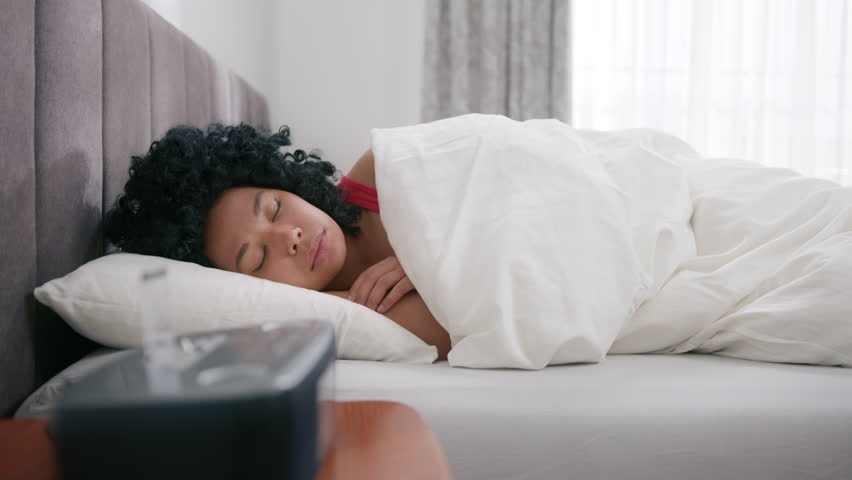 Sleepy black girl covers up in blanket and continue to sleep slow motion. African american female sleeping in bed wakes up early hour to disable activated digital alarm clock sounding on bedside table Royalty-Free Stock Footage #1099414865