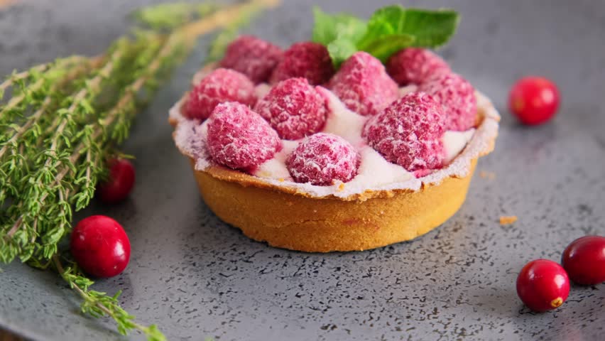 Raspberry tartlet with whipped cream and fresh berries served on a plate, slow motion rotation video, mini tart cake sprinkled with sugar, close up video of sweet dessert, hd video footage Royalty-Free Stock Footage #1099416515