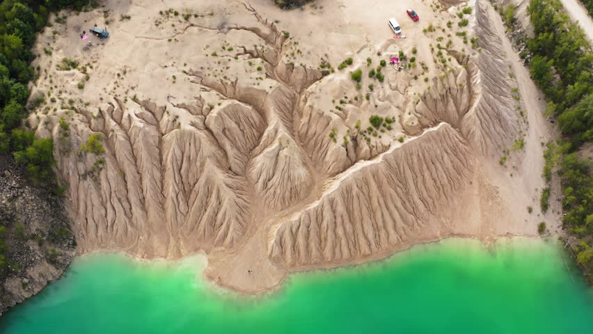 Industrial neon-colored lake with yellowish soil as seen from above. Aerial view of people enjoying picturesque vistas from the top of the cliff. High quality 4k footage