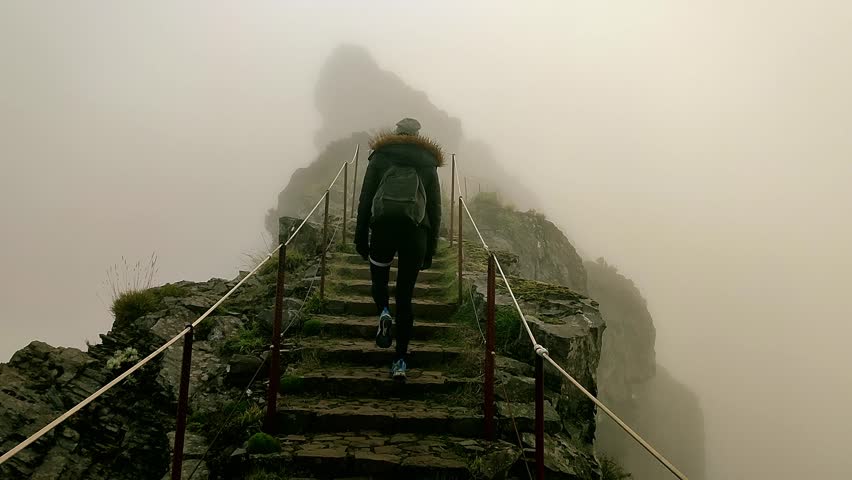 Woman hiker climbs the foggy stairs. Young and fit woman is walking up the trail to the top of Pico do Arieiro, Madeira. Tired woman walking and hiking stone stairs. Fog and mist in the mountains.  | Shutterstock HD Video #1099431987
