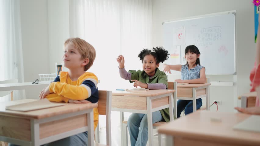 Elementary school students are sitting in the classroom at school and are raising their hands when the teacher asks Royalty-Free Stock Footage #1099433131