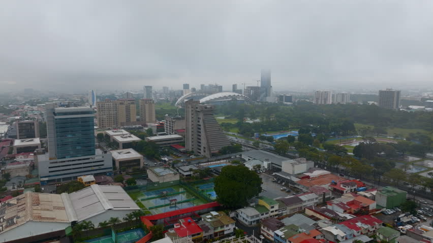 Forwards fly above town development on rainy day. Urban borough and a Sabana Park with national stadium. San Jose, Costa Rica
