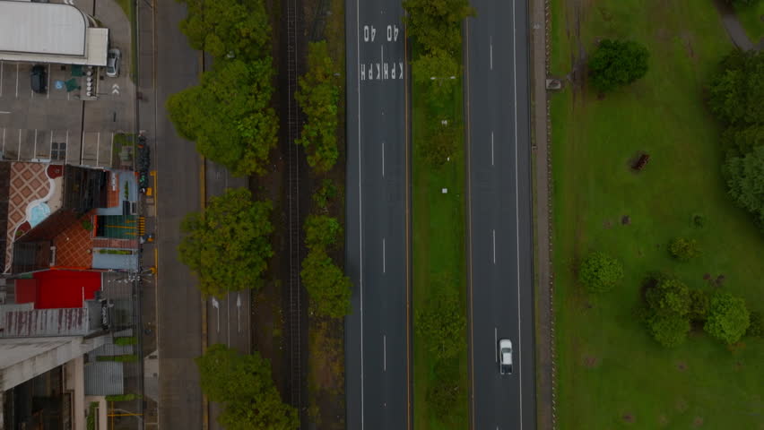 Birds eye shot of transport infrastructure in town. Cars passing road intersection and road leading along with rail track. San Jose, Costa Rica