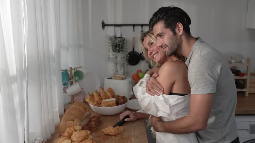 Romantic couple warmly hugging and kissing each other in the kitchen at home in the morning. | Shutterstock HD Video #1099437117