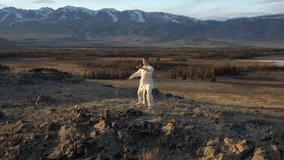 Video of kungfu master in a white sports uniform training on the hill. Man perform wushu forms in nature on background of pavilion, Sun rays  and snowy mountains at sunset time. 
