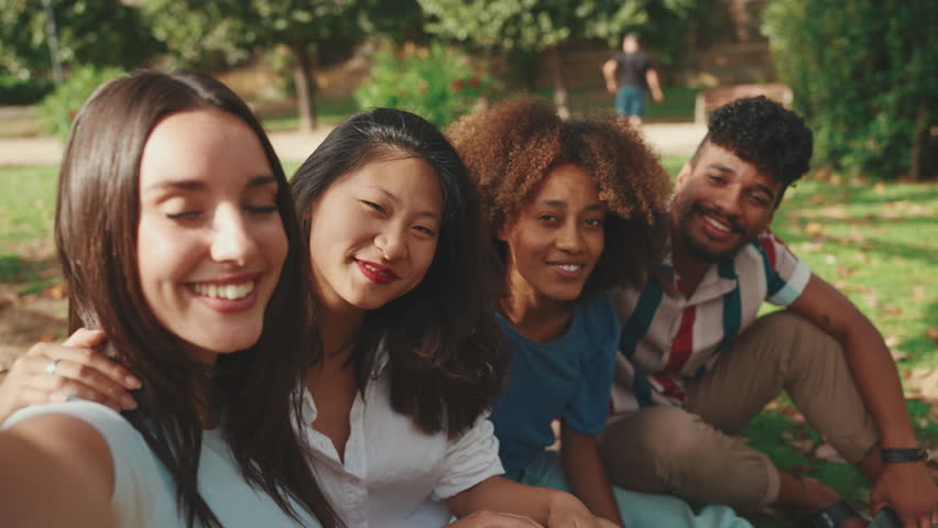 Close-up of happy young people are looking at taking selfie on summer day outdoors. Group of smiling friends posing at smartphone camera Royalty-Free Stock Footage #1099438859