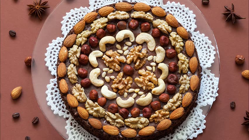 Flat lay of homemade chocolate cake decorated with different types of nuts and fragrant spices on brown background. Top view, close-up, mock up
